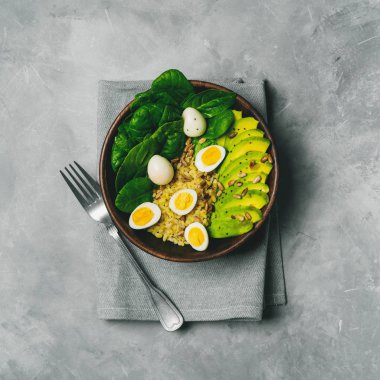 Beton zemin üzerine ahşap kase yumurta salatası bulgur, ıspanak, avokado ve bıldırcın görünümü Kapat