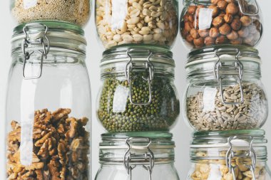 Görünümü Kapat cam kavanozlar ile kaşu, fındık, ceviz, fıstık, mung fasulye, quinoa, ışık arka plan ayçiçeği tohumu