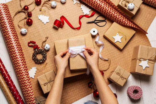 Верхний вид женских рук, обертывающих подарочную коробку с упаковочной лентой, веревкой, бумажными рулонами и декорациями на оберточной бумаге
