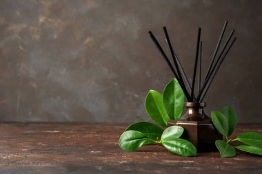 Aroma reed diffuser bottle with rattan sticks and green leaves on dark brown background clipart
