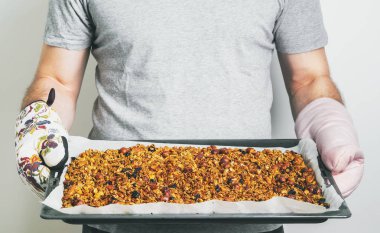 Yulaf ezmesi, badem, kaju fıstığı, fıstık, fındık, ayçiçeği tohumu üzerinden Ev yapımı granola ile fırın tepsisi üzerinde açık renkli holding holding adam görünümü Kapat 