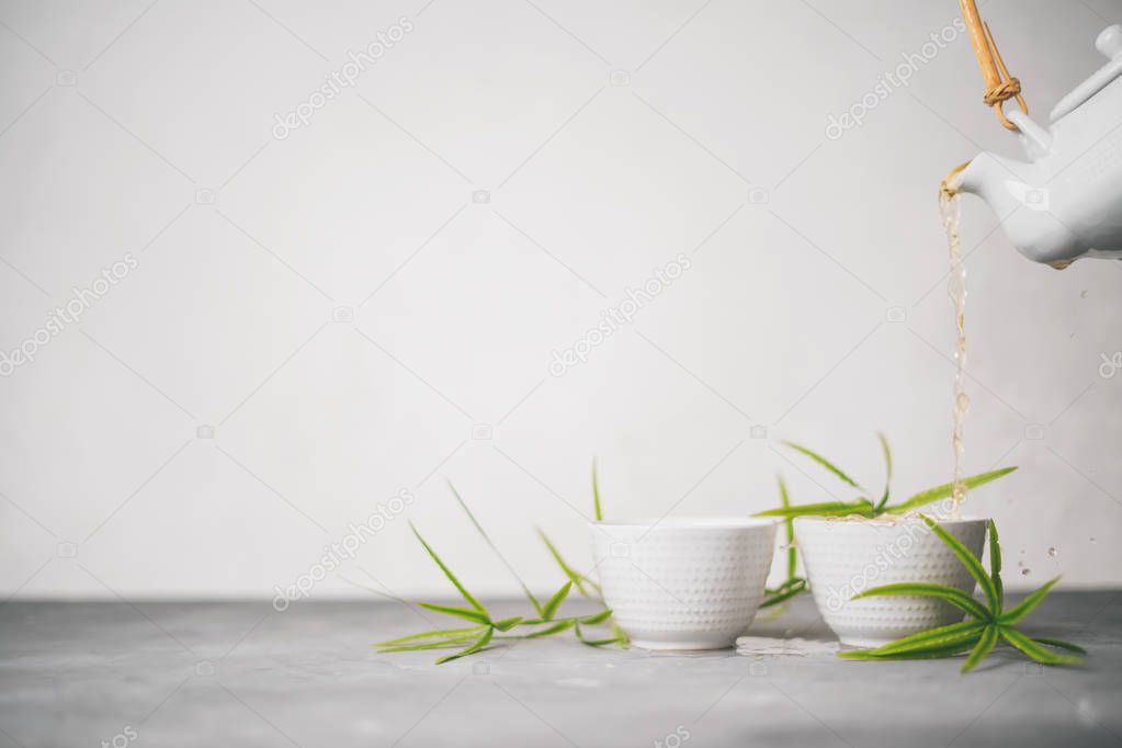 Female hand pouring green tea from a teapot into cups on white background with copy space. Asian tea set. 
