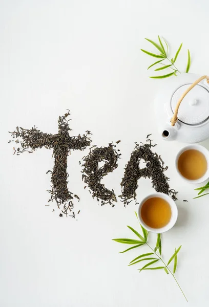 Composition tea set with lettering TEA made of dry tea leaves with teapot, cups and leaves on white background