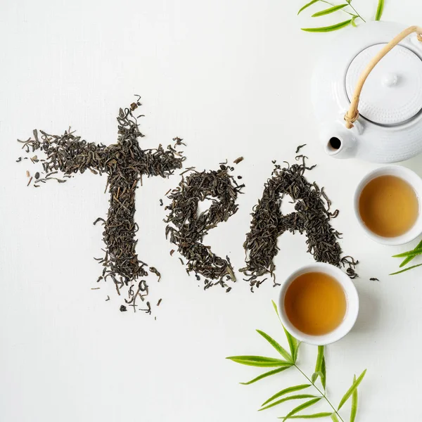 Composition tea set with lettering TEA made of dry tea leaves with teapot, cups and leaves on white background