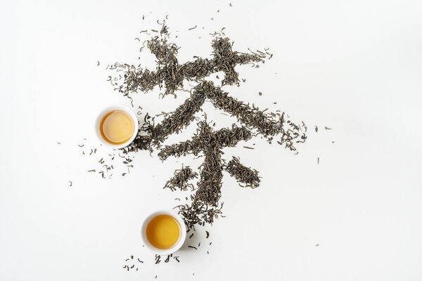 Traditional Chinese hanzi Calligraphy "Tea" stowed by tea on white fabric surface.