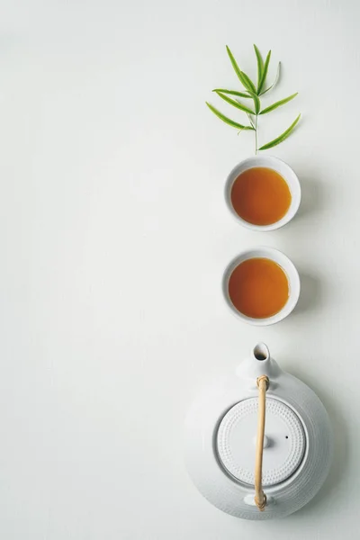 白色的茶和茶壶 周围是白色背景上的绿色竹叶 — 图库照片
