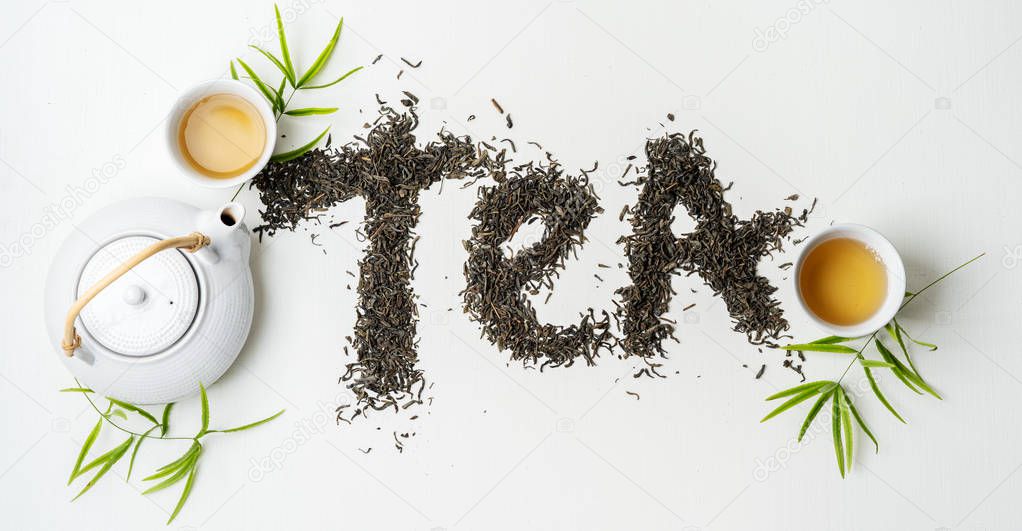 Composition tea set with lettering TEA made of dry tea leaves with teapot, cups and leaves on white background