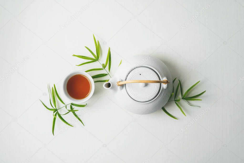 Asian tea concept, two white cups of tea and teapot surrounded with green tea dry leaves view from above, space for a text on white fabric background