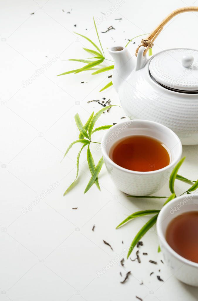 Asian set with green tea, cups and teapot on white background with green leaves 