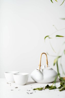 Işık gri arka plan üzerinde Asya çay seti ile iki beyaz bardak çay ve yeşil çay kuru ile çevrili çaydanlık yaprakları