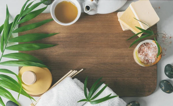Açık yüzeyde ahşap tahta ile çay seti, beyaz havlu, aroma kokusu, organik sabunlar, yağ, pembe tuz ve palmiye yaprakları ile çerçeve kompozisyonu