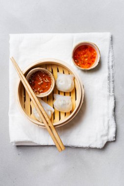 Geleneksel Çince köfte Dim toplamları Har Gow sos ve yemek çubukları ile bambu gemi içinde ışık arka plan üzerinde buğulama