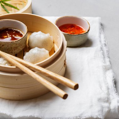 Geleneksel Çince köfte Dim toplamları Har Gow sos ve yemek çubukları ile bambu gemi içinde ışık arka plan üzerinde buğulama