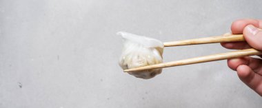 Dim Sum Har Gow ile tarafından çubuk üzerinde buharda pişmiş geleneksel Çin böreği tutan bir el ile yakın çekim. Asya gıda arka plan.