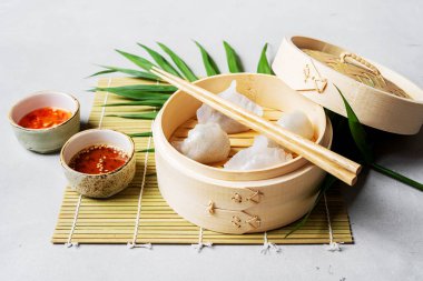Geleneksel Çince köfte Dim toplamları Har Gow sos ve yemek çubukları ile bambu gemi içinde ışık arka plan üzerinde buğulama