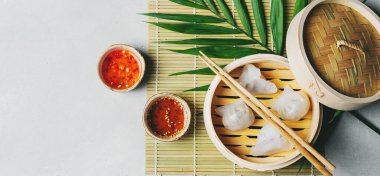 Geleneksel Çince köfte Dim toplamları Har Gow sos ve yemek çubukları ile bambu gemi içinde ışık arka plan üzerinde buğulama