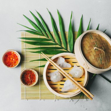 Geleneksel Çince köfte Dim toplamları Har Gow sos ve yemek çubukları ile bambu gemi içinde ışık arka plan üzerinde buğulama