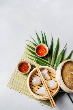 Geleneksel Çince köfte Dim toplamları Har Gow sos ve yemek çubukları ile bambu gemi içinde ışık arka plan üzerinde buğulama