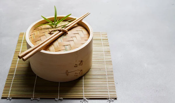 Traditional chinese bamboo steamer for steamed dumplings Dim Sums with chopsticks on light surface with copy space. Asian food background.