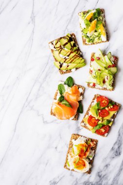 protein toast with delicious avocado, salmon, eggs, vegetables, tomatoes, herbs, pine nuts, sunflower seeds and cream cheese on marble surface clipart