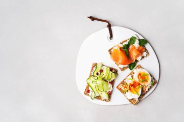 Superfood protein ekmek üstüne lezzetli Topingler ile: avokado, somon balığı, yumurta, sebze, domates, otlar, çam fıstığı, ayçiçeği tohumu ve mermer üzerine krem peynir. Sağlıklı beslenme kavramı kopya alanı ile.
