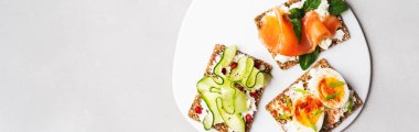 Superfood protein ekmek üstüne lezzetli Topingler ile: avokado, somon balığı, yumurta, sebze, domates, otlar ve krem peynir üzerinde mermer serface. Uzun geniş afiş kopya alanı ile. Sağlıklı beslenme kavramı