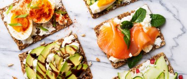 Superfood protein ekmek üstüne lezzetli Topingler ile: avokado, somon balığı, yumurta, sebze, domates, otlar ve krem peynir üzerinde mermer serface. Uzun geniş afiş kopya alanı ile. Sağlıklı beslenme kavramı