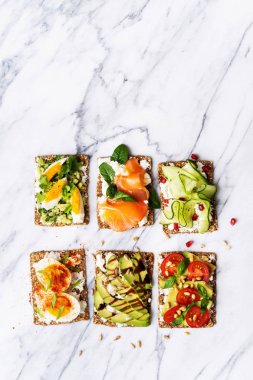 protein tost lezzetli avokado, somon balığı, yumurta, sebze, domates, otlar, çam fıstığı, ayçiçeği tohumu ve krem peynir mermer yüzeyi ile