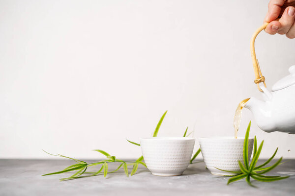 Female hand pouring green tea from a teapot into cups on white background with copy space. Asian tea set. 