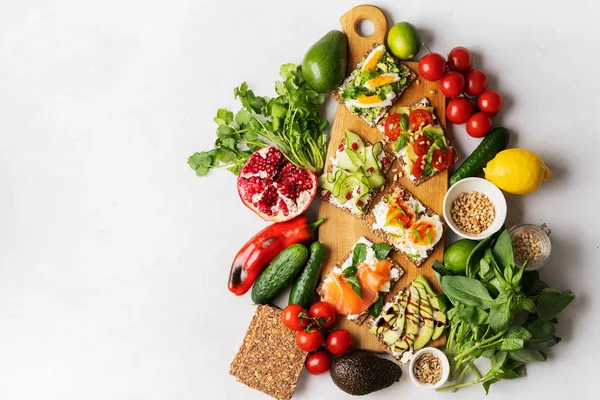 Ana sayfa görünümü Superfood protein ekmek üstüne lezzetli Topingler ile: füme somon, ıspanak, salatalık, domates, sebze malzemeler arasında ahşap uzun kesme tahtası üzerinde krem peynir. sağlıklı atıştırmalıklar.