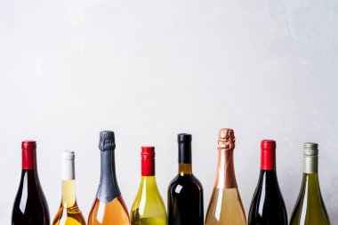 Tops from different kinds new bottles of champagne, white, red wine on light background clipart