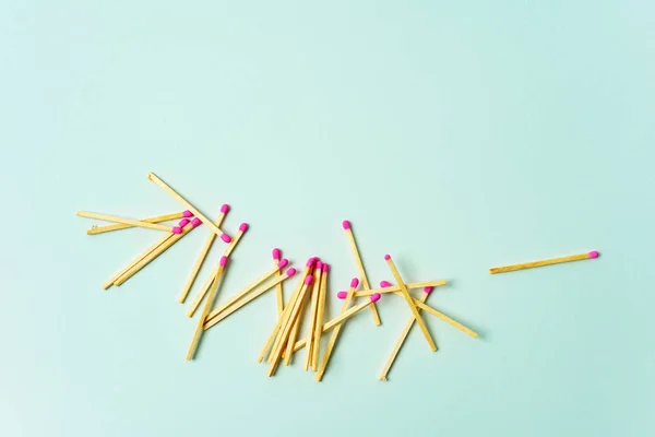 Pile of wooden matches with pink heads scattered on turquoise pastel background