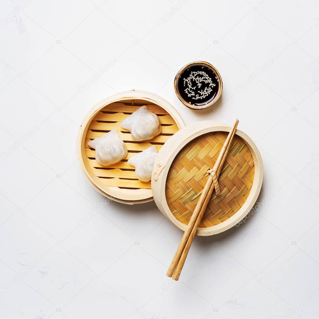 Traditional chinese steamed dumplings Dim Sums in bamboo steamer with sauces and chopsticks on light background