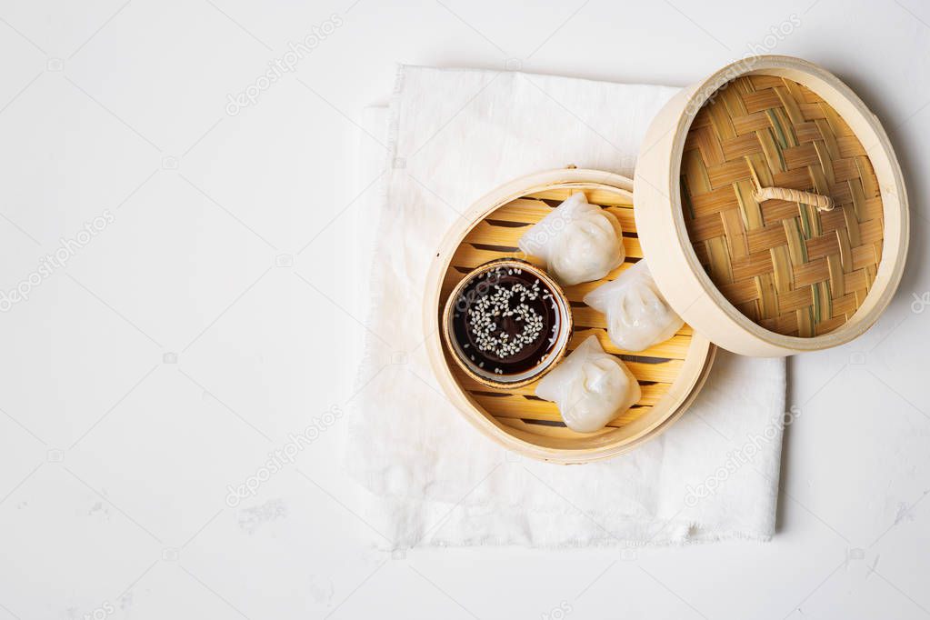 Traditional chinese steamed dumplings Dim Sums in bamboo steamer with sauce on light surface