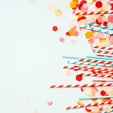Renkli konfeti ile pastel arka planda kırmızı ve mavi pipetler yığını