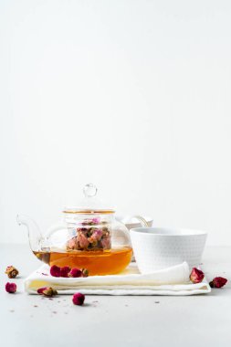 iki beyaz bardak ve gri taş arka planda kurutulmuş pembe gül tomurcukları bitkisel çay ile şeffaf çaydanlık