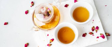 iki beyaz bardak ve gri taş arka planda kurutulmuş pembe gül tomurcukları bitkisel çay ile şeffaf çaydanlık