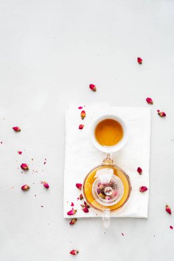 Beyaz seramik fincan ve gri arka planda kurutulmuş pembe güller bitkisel çay ile şeffaf çaydanlık