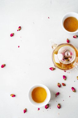iki beyaz bardak ve gri taş arka planda kurutulmuş pembe gül tomurcukları bitkisel çay ile şeffaf çaydanlık