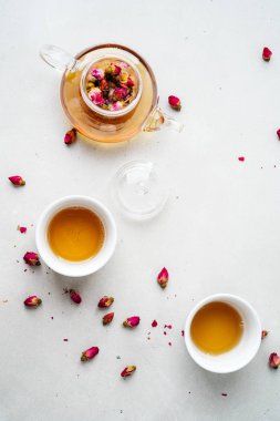 iki beyaz bardak ve gri taş arka planda kurutulmuş pembe gül tomurcukları bitkisel çay ile şeffaf çaydanlık