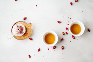 iki beyaz bardak ve gri taş arka planda kurutulmuş pembe gül tomurcukları bitkisel çay ile şeffaf çaydanlık