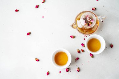 iki beyaz bardak ve gri taş arka planda kurutulmuş pembe gül tomurcukları bitkisel çay ile şeffaf çaydanlık