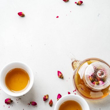 iki beyaz bardak ve gri taş arka planda kurutulmuş pembe gül tomurcukları bitkisel çay ile şeffaf çaydanlık