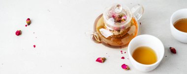 iki beyaz bardak ve gri taş arka planda kurutulmuş pembe gül tomurcukları bitkisel çay ile şeffaf çaydanlık