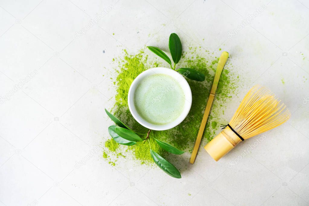 Organic green Matcha powder tea with chasen bamboo whisk, chashaku spoon and green leaves on light background