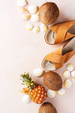 Pembe pastel arka plan üzerinde deri trendy parmak arası terlik, kabuklar ve tropikal meyvelerüst görünümü