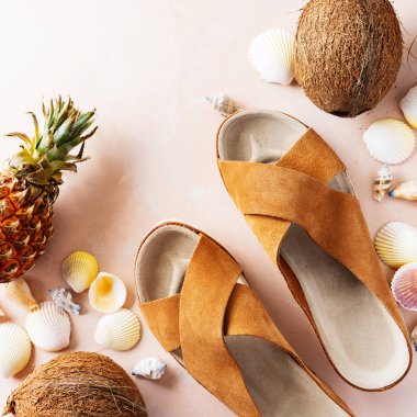 Pembe pastel arka plan üzerinde deri trendy parmak arası terlik, kabuklar ve tropikal meyvelerüst görünümü