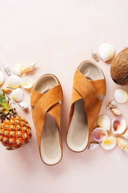 Pembe pastel arka plan üzerinde deri trendy parmak arası terlik, kabuklar ve tropikal meyvelerüst görünümü