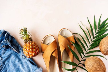 Şık deri sandalet, kot şort ve palmiye yaprağı ile pembe pastel arka plan üzerinde tropikal meyveler