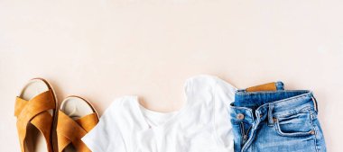 Pembe pastel arka plan üzerinde temel beyaz t-shirt, kot şort ve trendy deri sandalet